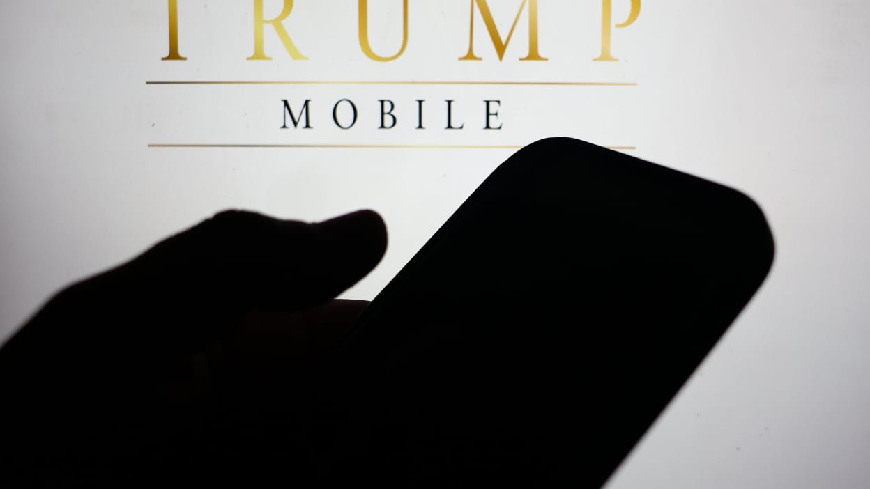 A shadow of a hand holding a phone in front of the Trump Mobile logo.