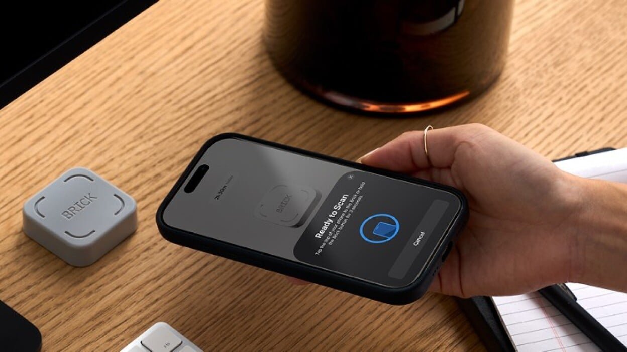 a person holds their phone to the brick device which sits on a desktop